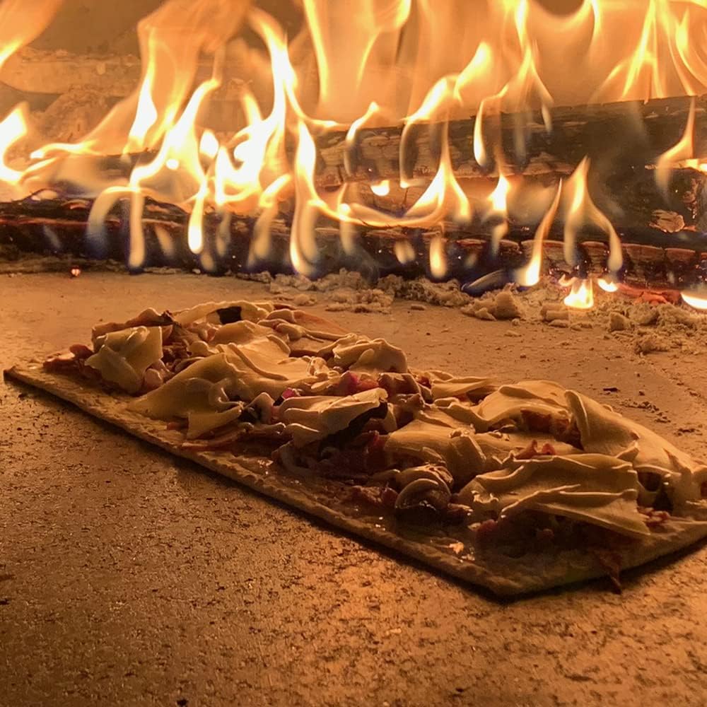A rectangular flatbread pizza with toppings is being baked on the stone surface of the high-performance Chicago Brick Oven CBO 1000 DIY Kit, which boasts a generous 53" x 39" cooking surface. Bright flames are seen in the background, giving the scene a warm, rustic ambiance.