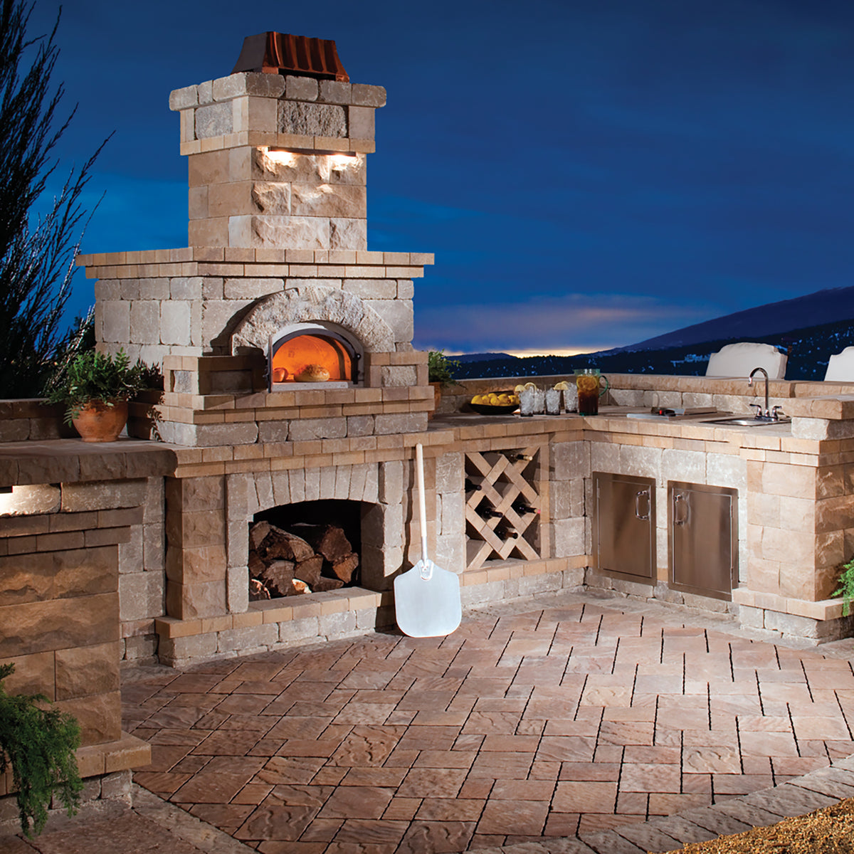 A Chicago Brick Oven glowing in a stone outdoor kitchen at dusk