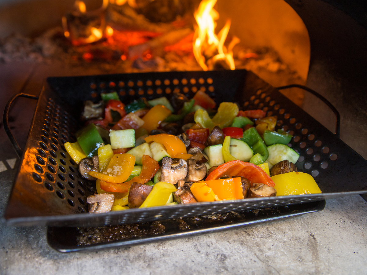 A basket of colourful vegetables roasting beside a wood fire