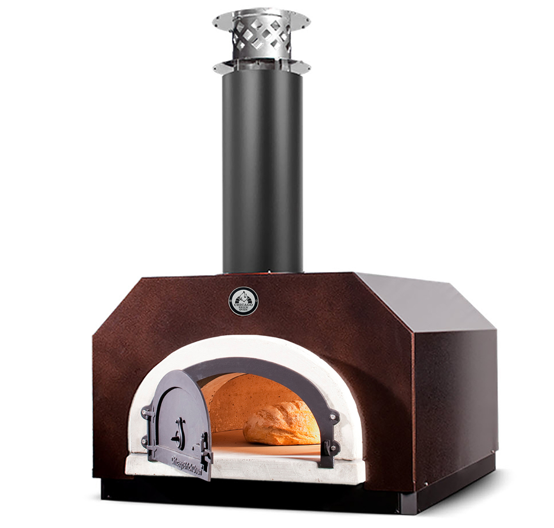 The CBO 500 Countertop Wood Fired Pizza Oven by Chicago Brick Oven features a compact, metal design with a visible chimney stack and is adorned in a striking dark brown finish. The outdoor wood-burning oven's front door stands open, revealing a loaf of bread baking inside, illuminated by the warm, golden glow from the fire within its 27" x 22" cooking surface.