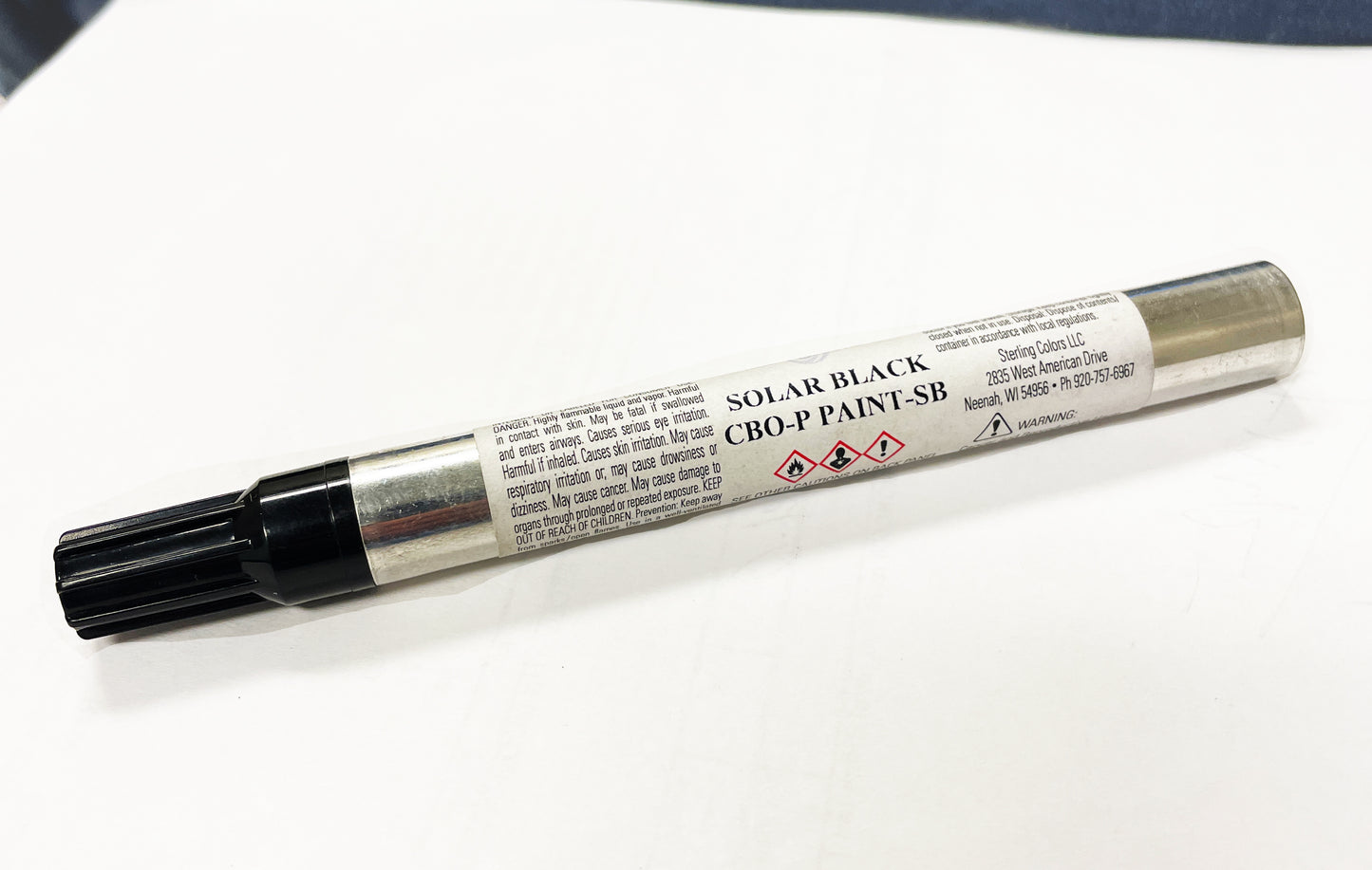 A metallic paint marker with a black cap is lying on a white surface. The label on the marker features "CHICAGO BRICK OVEN," "TOUCH-UP PAINT KITS," and safety icons indicating hazardous material, along with other small print. Ideal for touch-up paint tasks, this versatile marker ensures seamless coverage in Silver Vein or Copper Vein finishes.