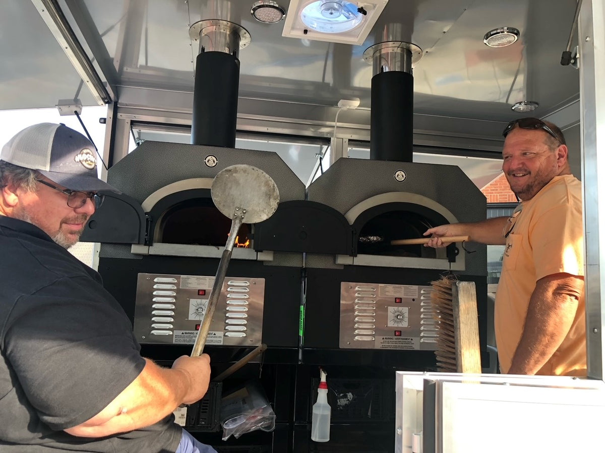 Two chefs with two Chicago Brick Oven Hybrid ovens installed side by side inside a food trailer
