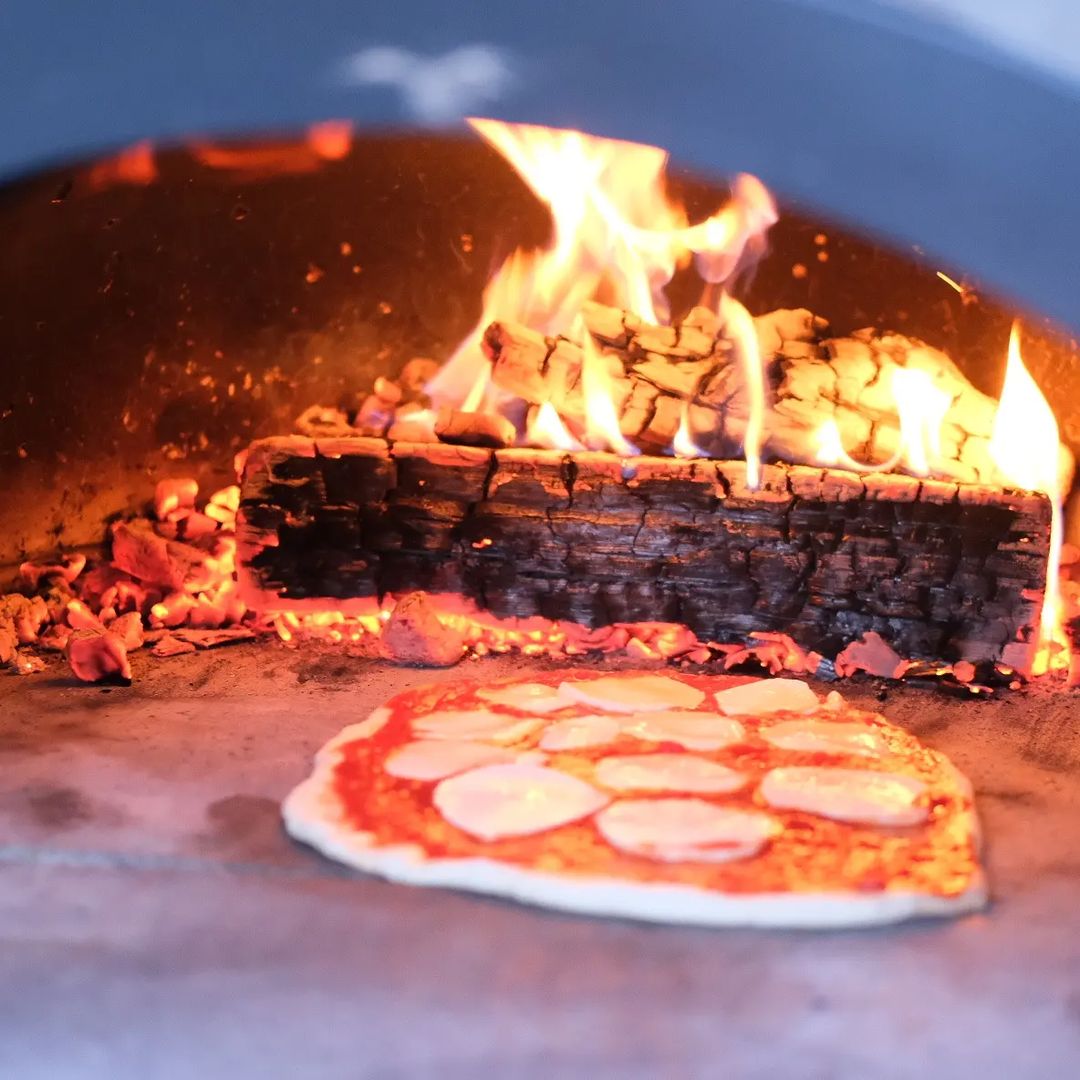 A CBO owner cooking beside a wood-fired oven