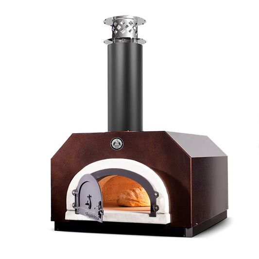 The Chicago Brick Oven CBO 500 Countertop Wood Fired Pizza Oven, featuring a 27" x 22" cooking surface, showcases a front-opening door and an overhead chimney. The oven glows with a lit fire inside, signaling its active use. Its dark brown body, accented by a white arch around the opening made of commercial-grade refractory cement, exudes a sturdy and rustic charm.